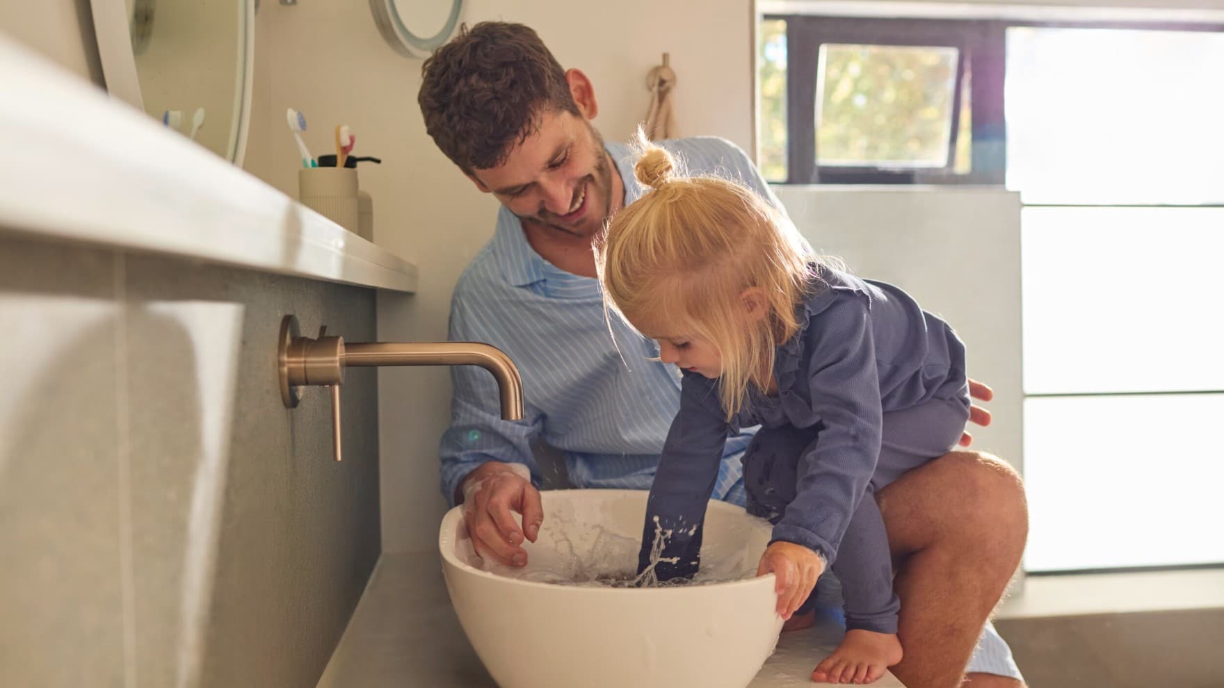Ein Vater und eine Tochter spielen mit Wasser in einem Waschbecken.