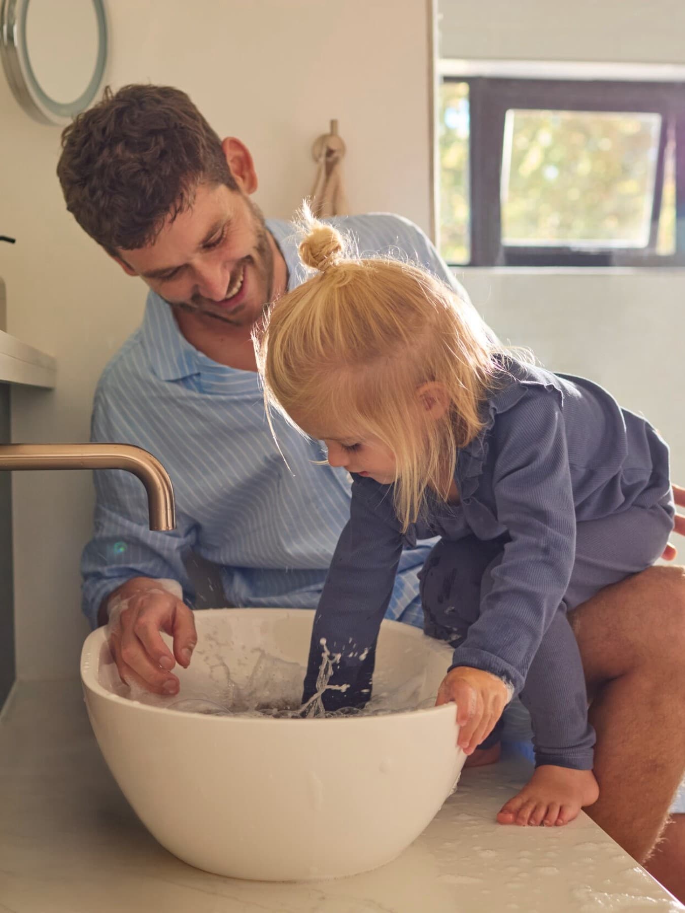 Ein Vater und eine Tochter spielen mit Wasser in einem Waschbecken.