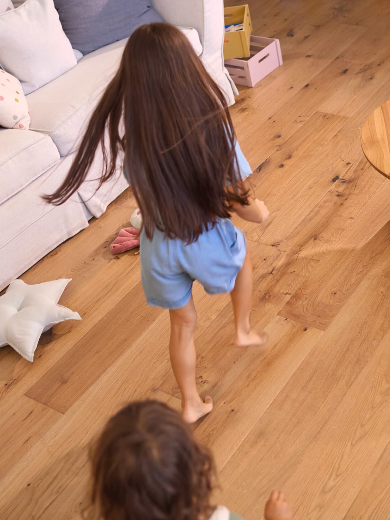 Zwei Kinder laufen barfuß über einen Holzboden zu Hause.