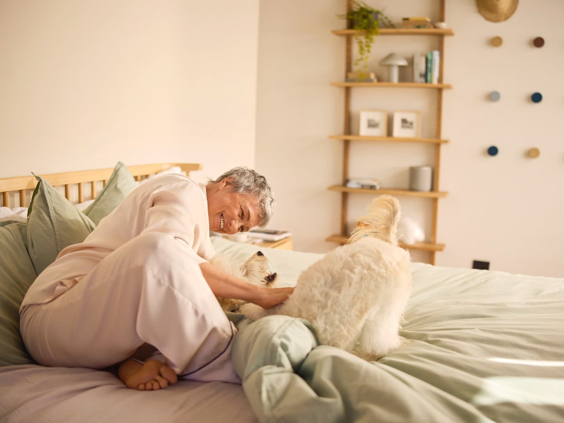 Eine lächelnde Frau, die einen Hund auf einem Bett streichelt