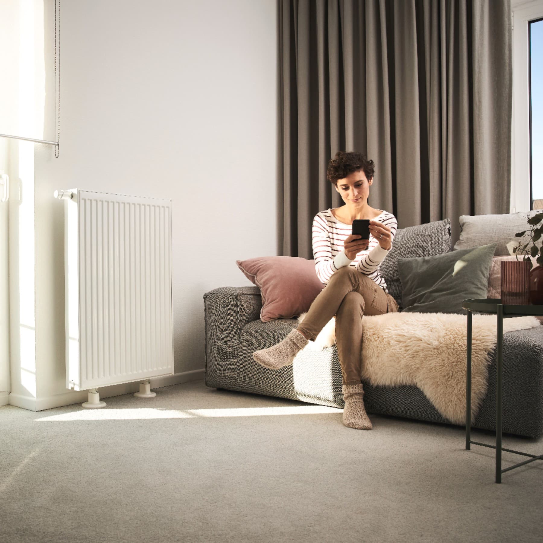 Frau sitzt mit Handy am Sofa