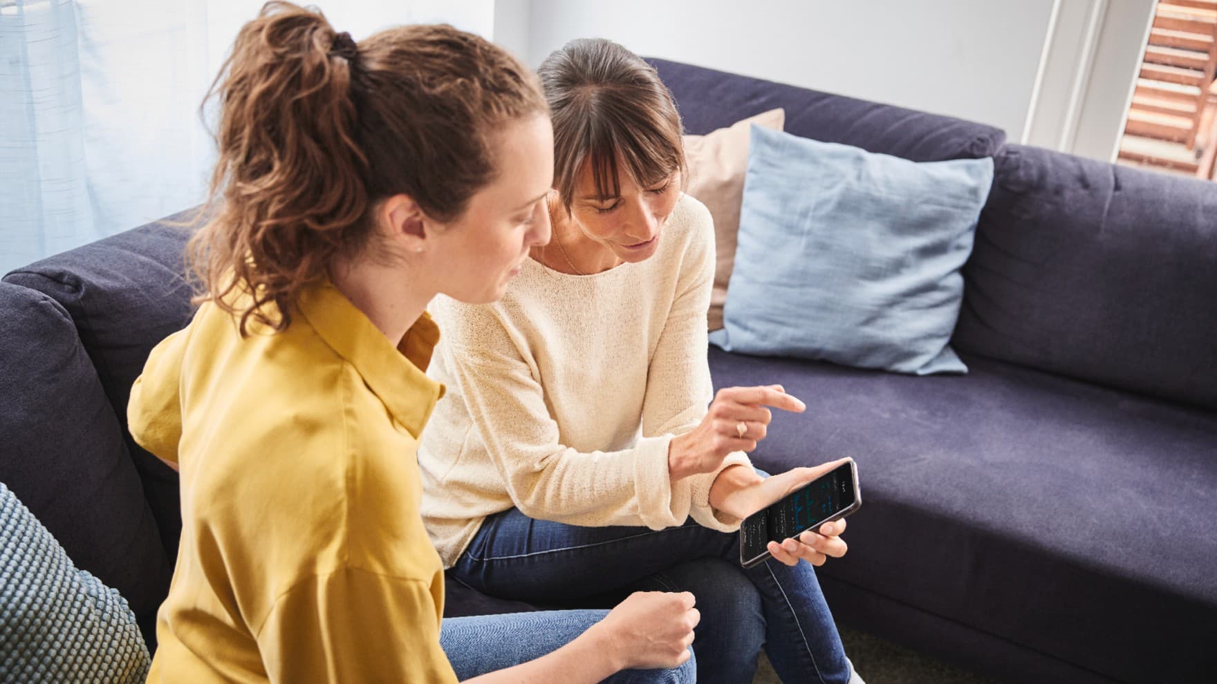 Zwei Frauen, die gemeinsam auf ein Smartphone gucken.