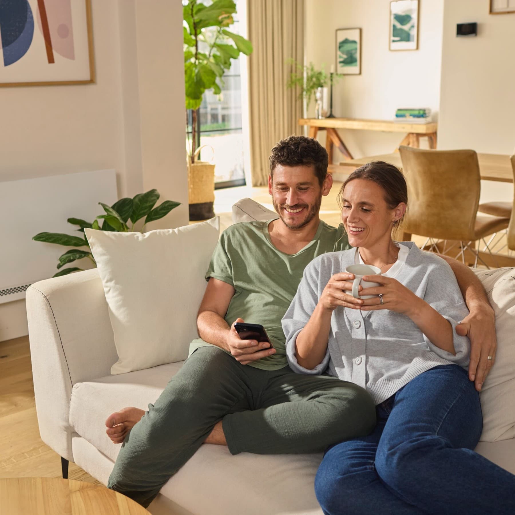 Mann und Frau sitzen auf einer Couch und schauen gemeinsam auf ein Handy