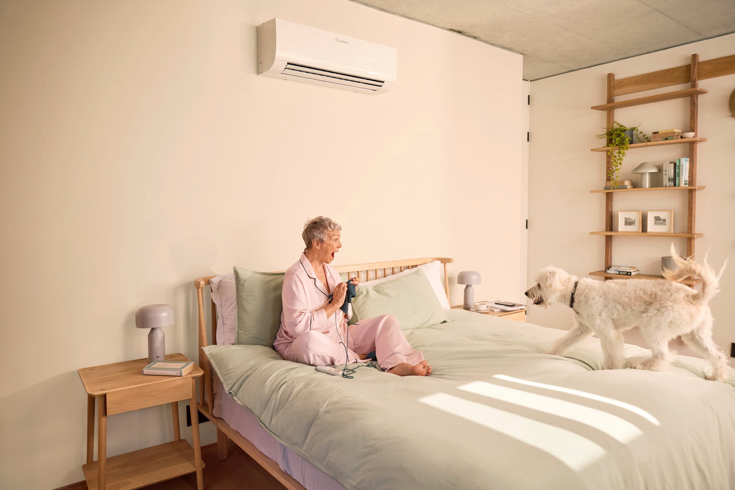 Eine Frau sitzt in ihrem Bett, als ihr Hund zu ihr kommt
