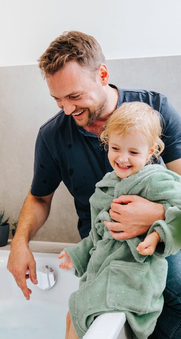 Vater und Kind sitzen neben der Badewanne.
