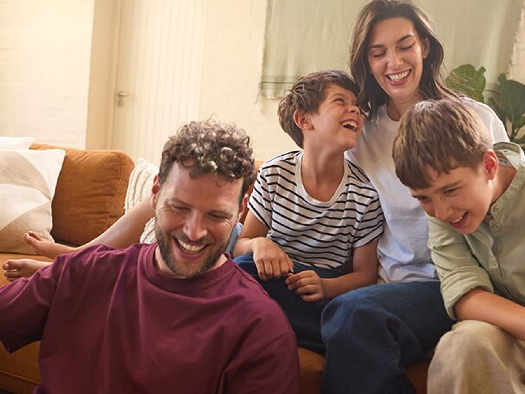 Familie sitzt im Wohnzimmer auf einem Sofa und lacht miteinander