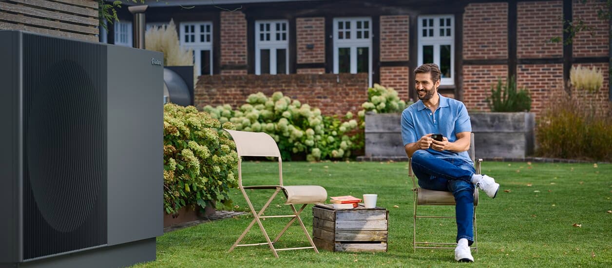 Ein Mann sitzt neben aroTHERM perform im Garten