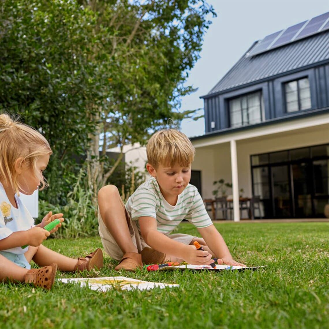 Kinder malen im Garten vor Haus mit Photovoltaik-Anlage