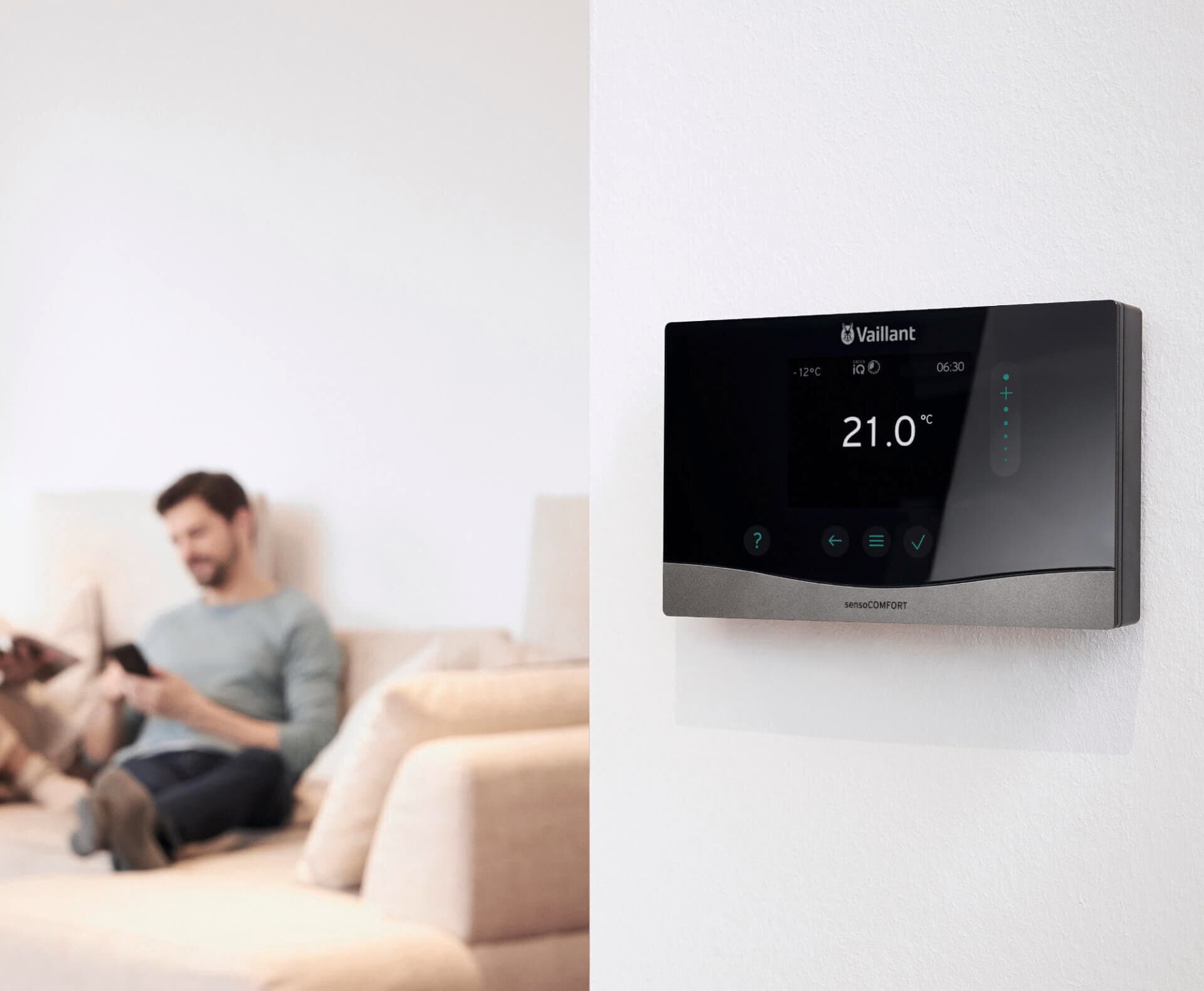 Ein Mann sitzt auf dem Sofa, an der Wand vor ihm hängt sensoCOMFORT