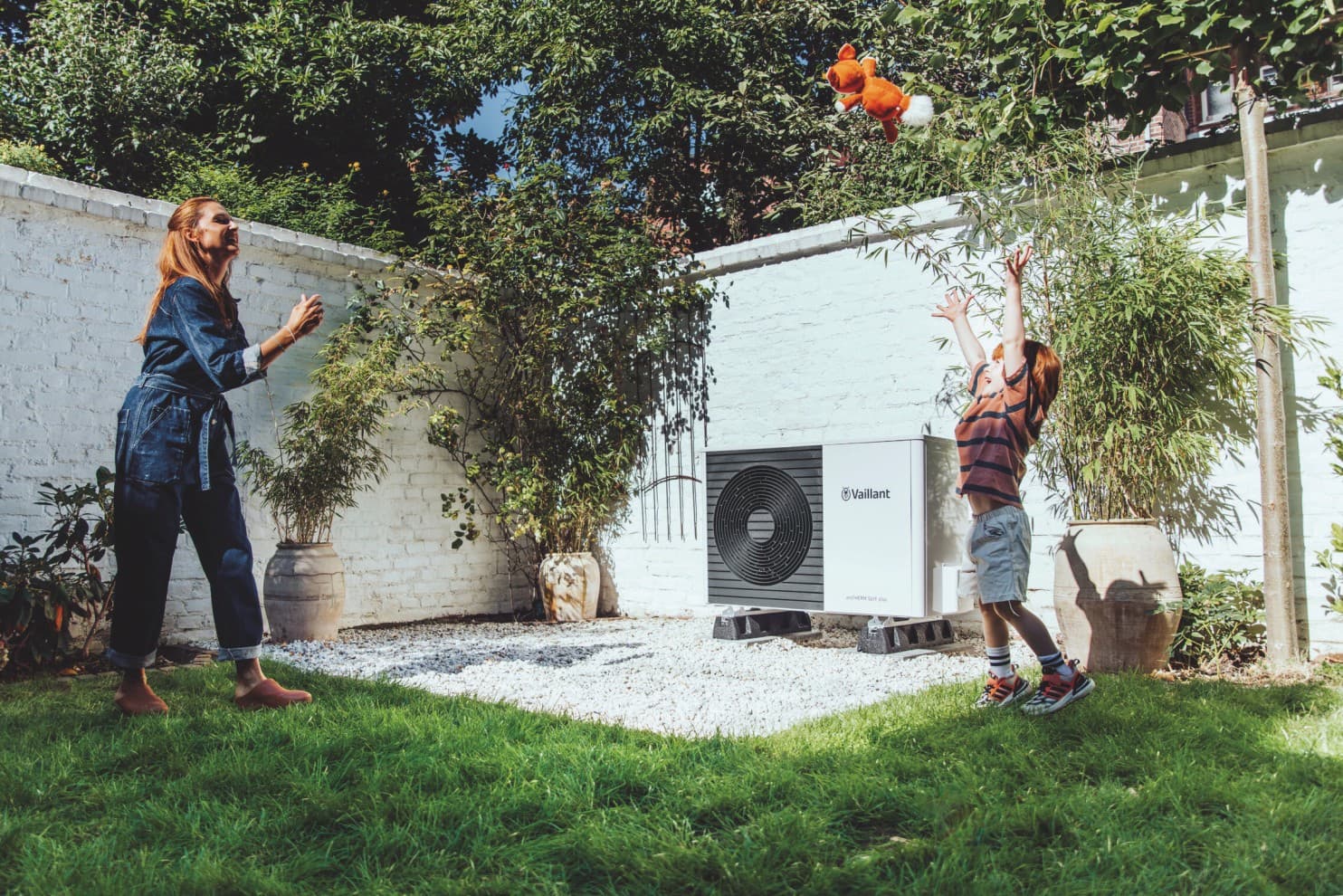 Frau und Kind spielen im Garten vor einer Wärmepumpe