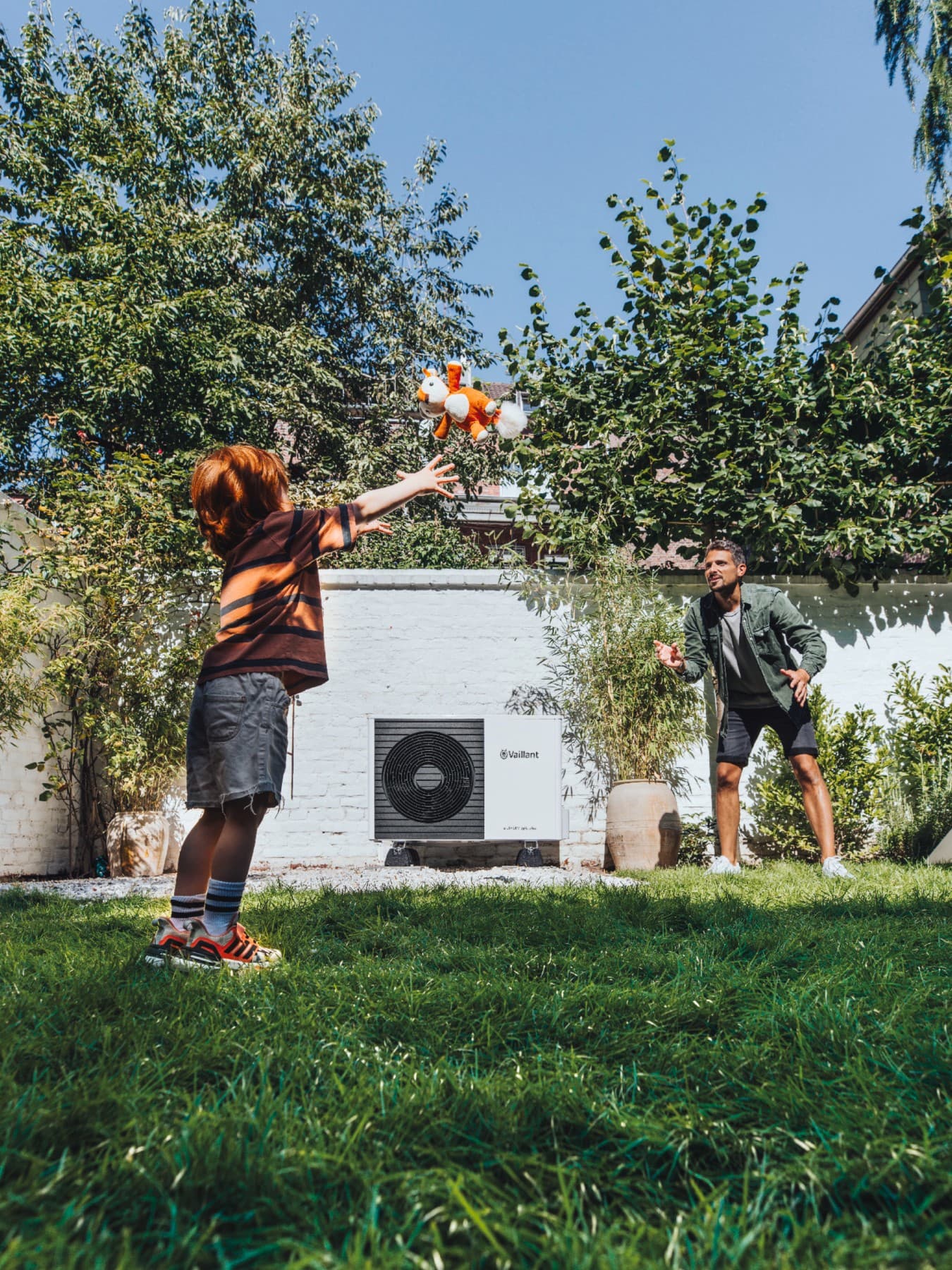 Kind spielt mit seinem Vater vor einer Wärmepumpe im Garten