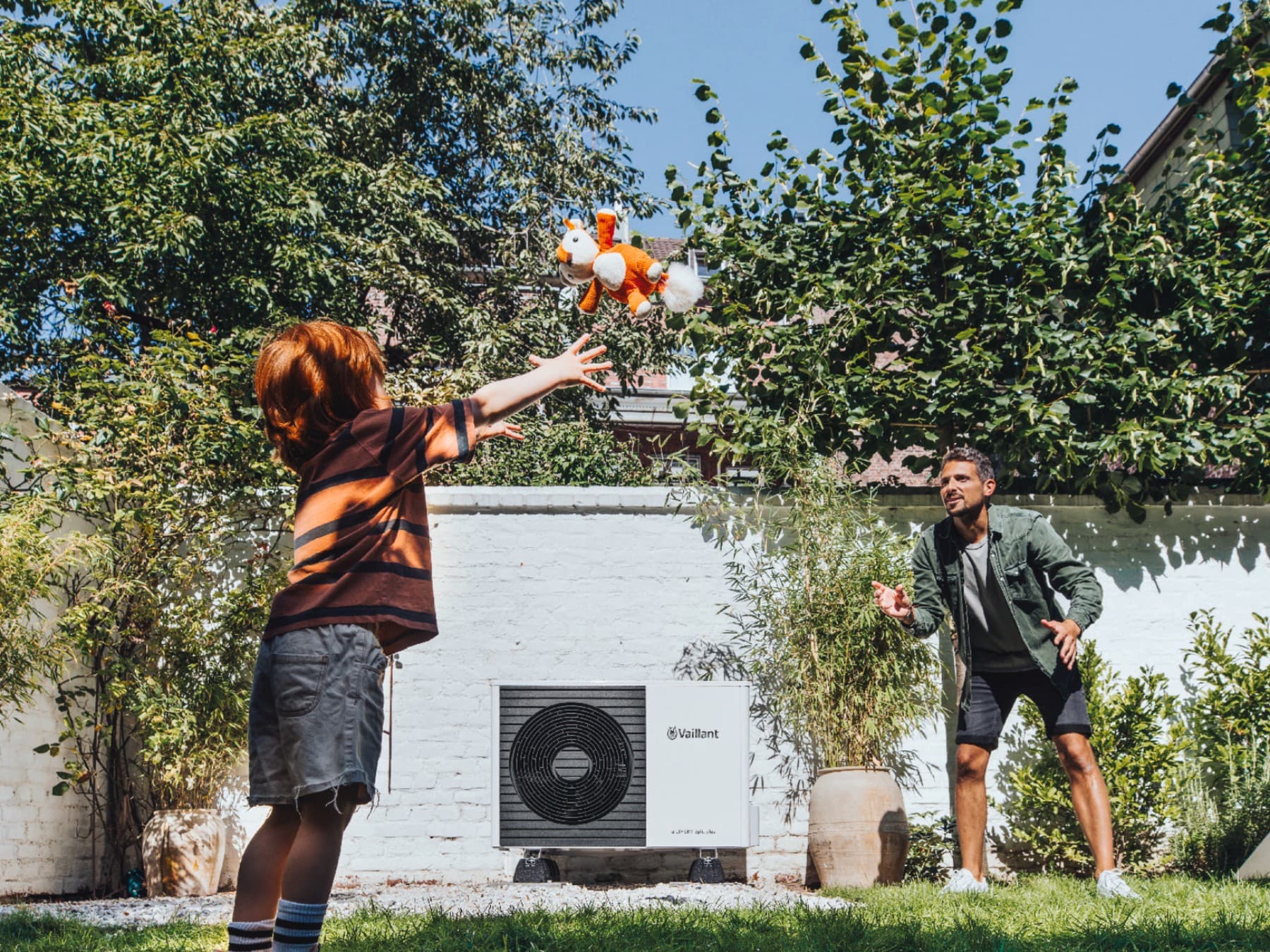 Kind spielt mit seinem Vater vor einer Wärmepumpe im Garten