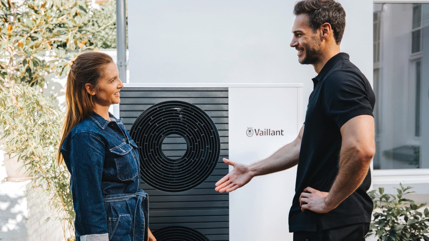 Ein Installateur und ein Kunde stehen vor einer Wärmepumpe und unterhalten sich.