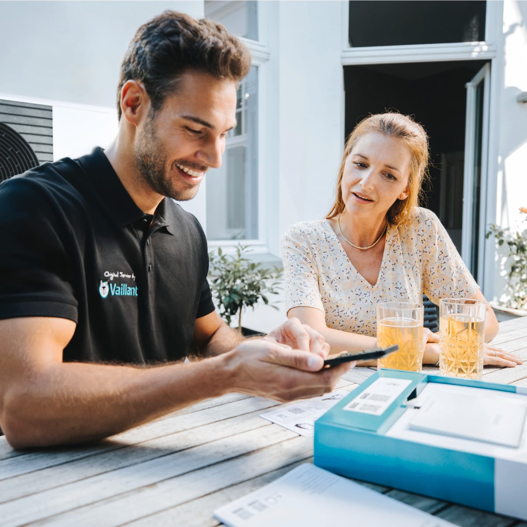 Vaillant Installateur mit einem Smartphone in der Hand und einem Kunden, der neben ihm sitzt