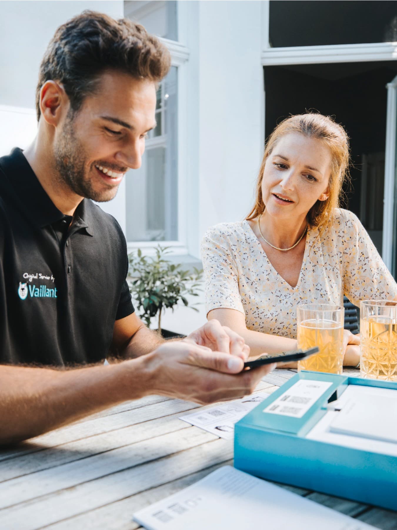 Vaillant Installateur mit einem Smartphone in der Hand und einem Kunden, der neben ihm sitzt