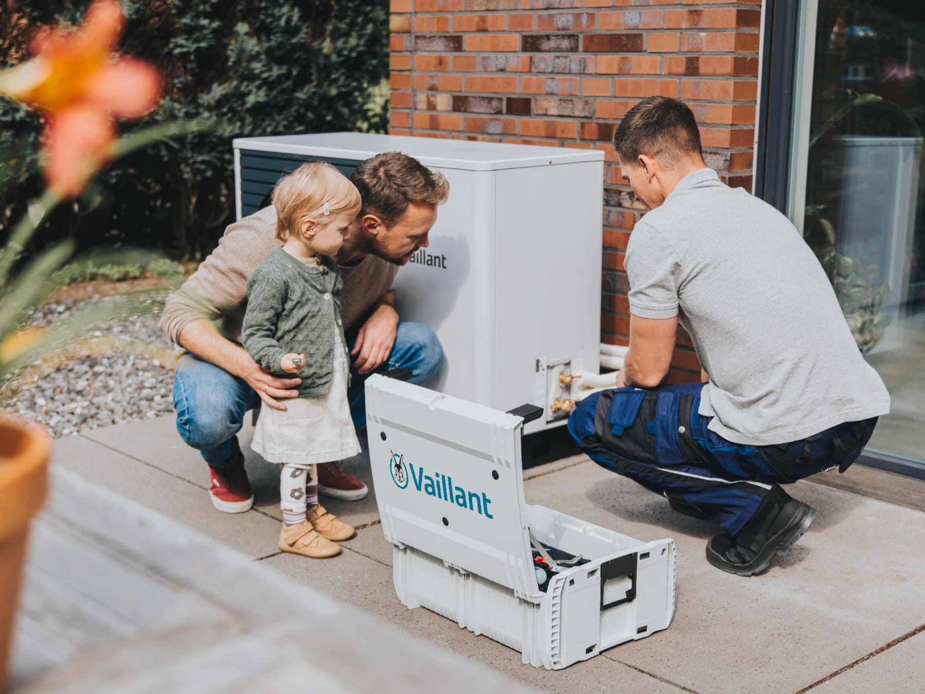 Ein Vater und seine Tochter beobachten einen Installateur beim Einbau einer Wärmepumpe.
