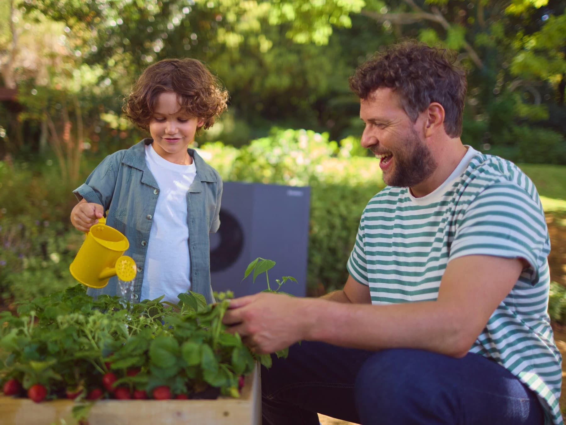 Mann mit seinem Sohn beim Gärtnern. Außeneinheit einer Wärmepumpe im Garten