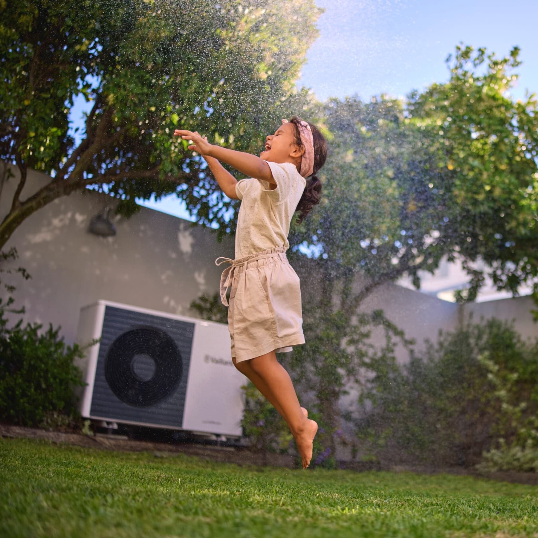 Mädchen spielt und springt im Garten vor einer Wärmepumpe
