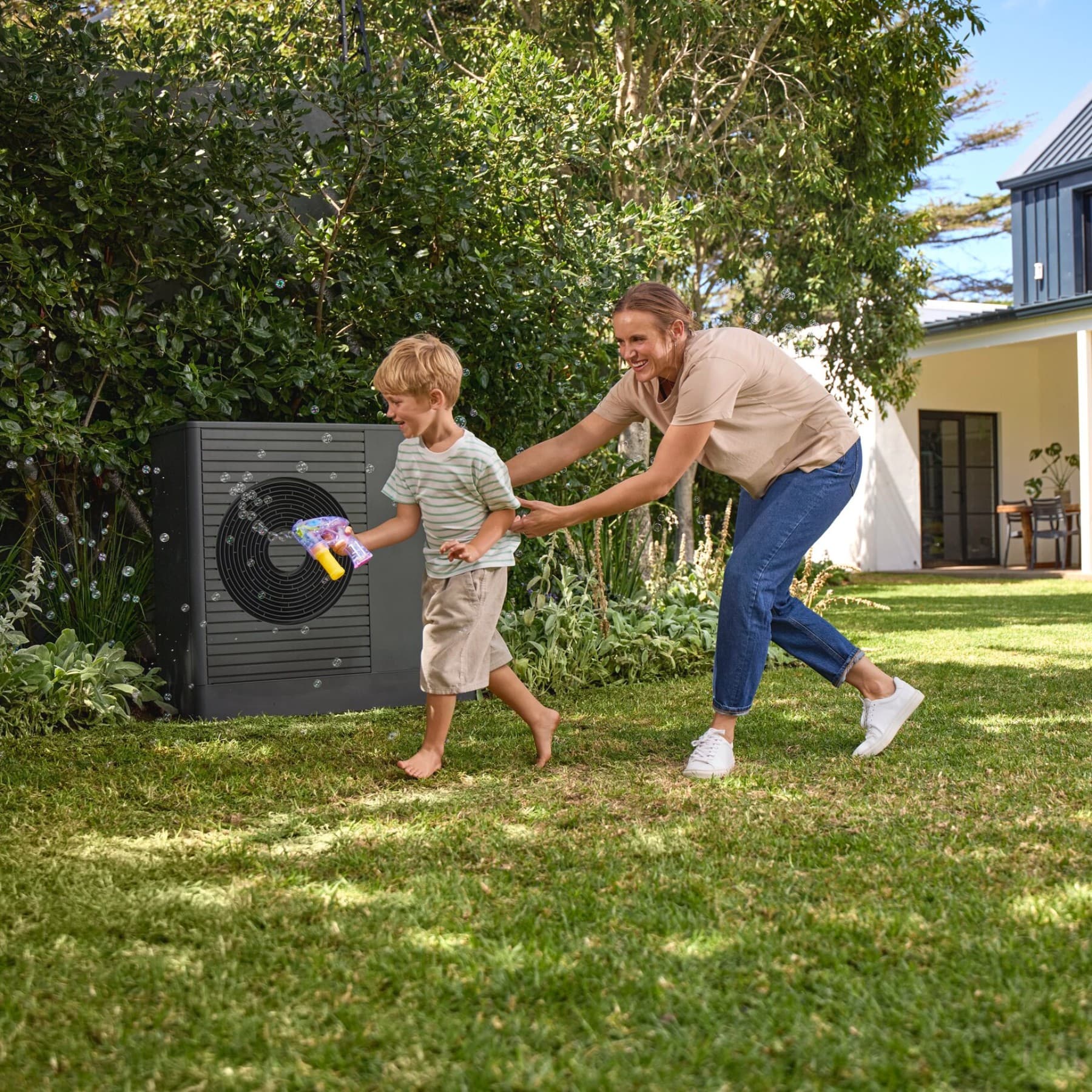 Kind und Mann spielen Ball im Garten vor einer Wärmepumpe