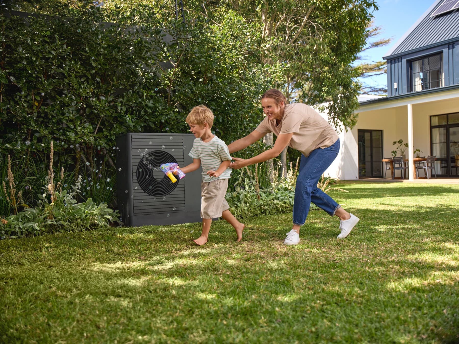 Kind und Mann spielen Ball im Garten vor einer Wärmepumpe