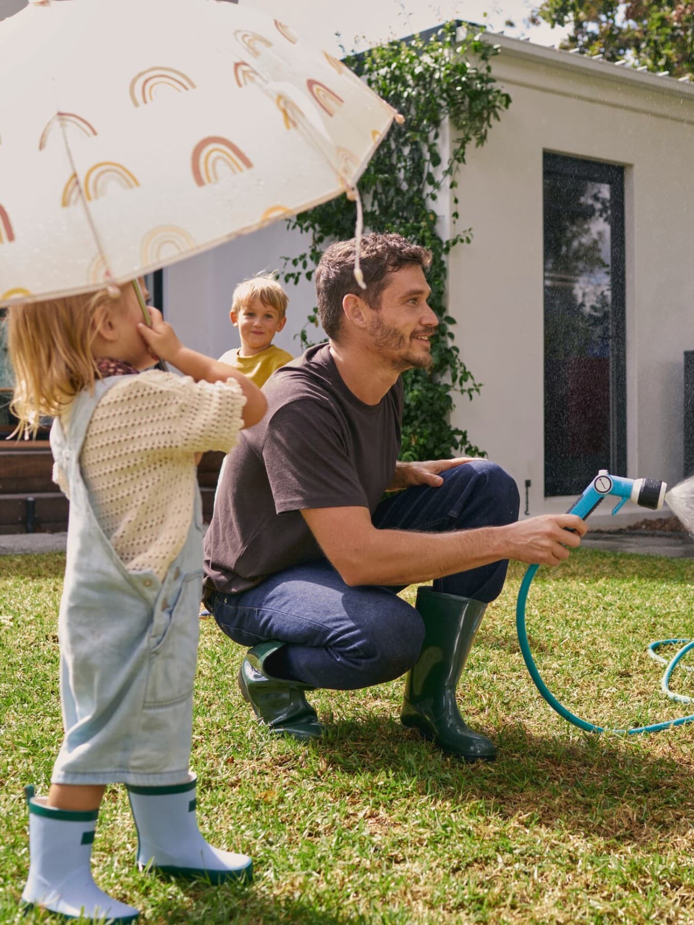Vater gießt zusammen mit den Kindern die Blumen im Garten vor einer Wärmepumpe