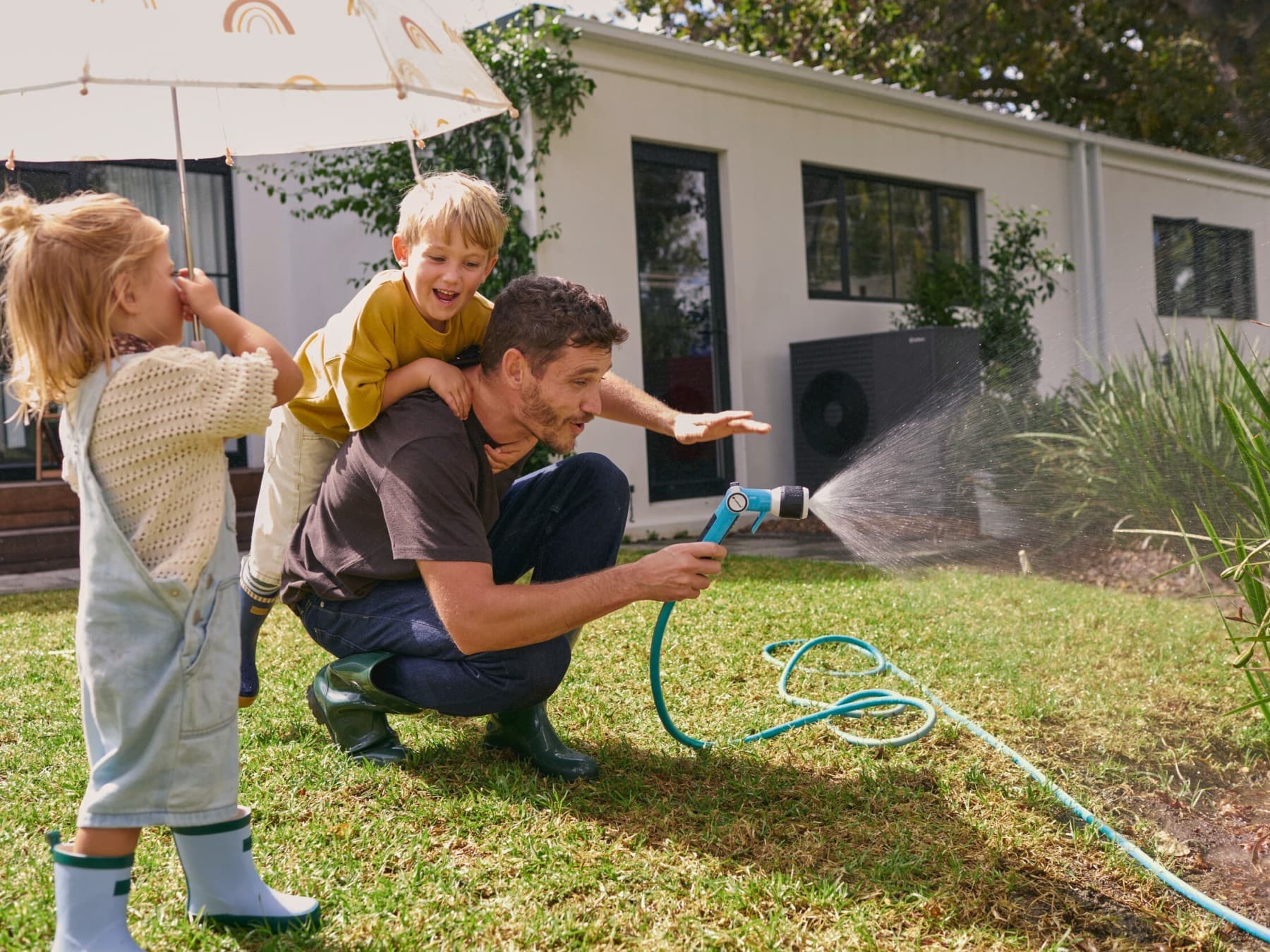 Vater und zwei Kinder spritzen mit einem Gartenschlauch Wasser