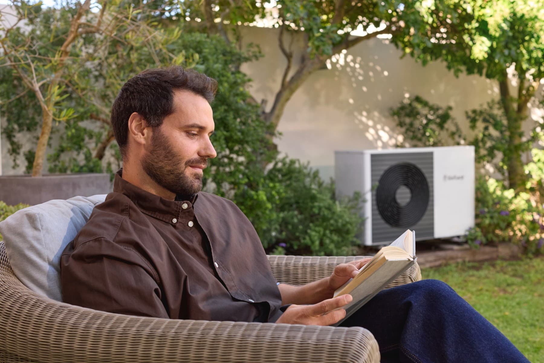 Mann liest Buch im Garten vor einer Wärmepumpe