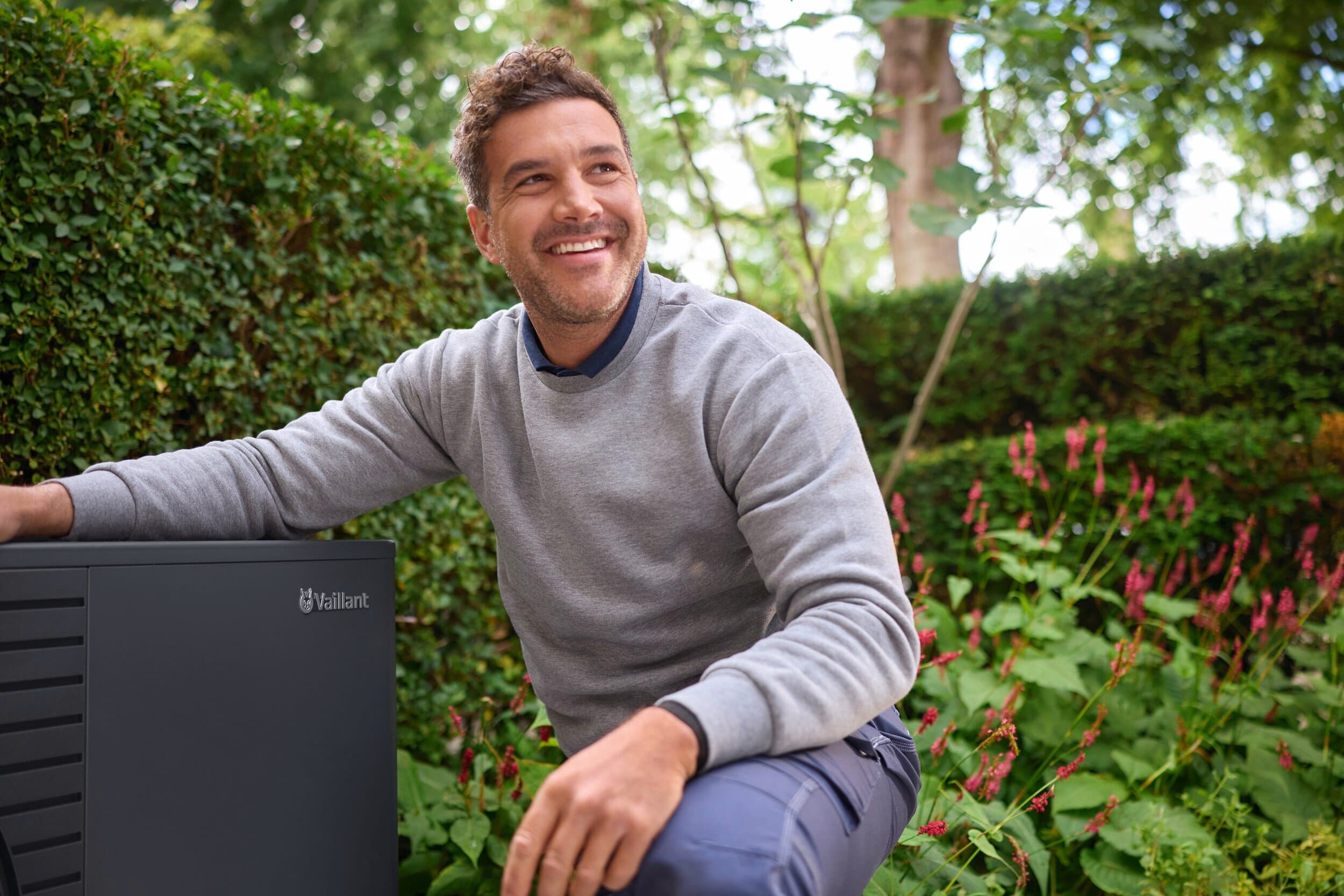 Ein Mann, der neben einem aroTHERM pro im Garten kniet