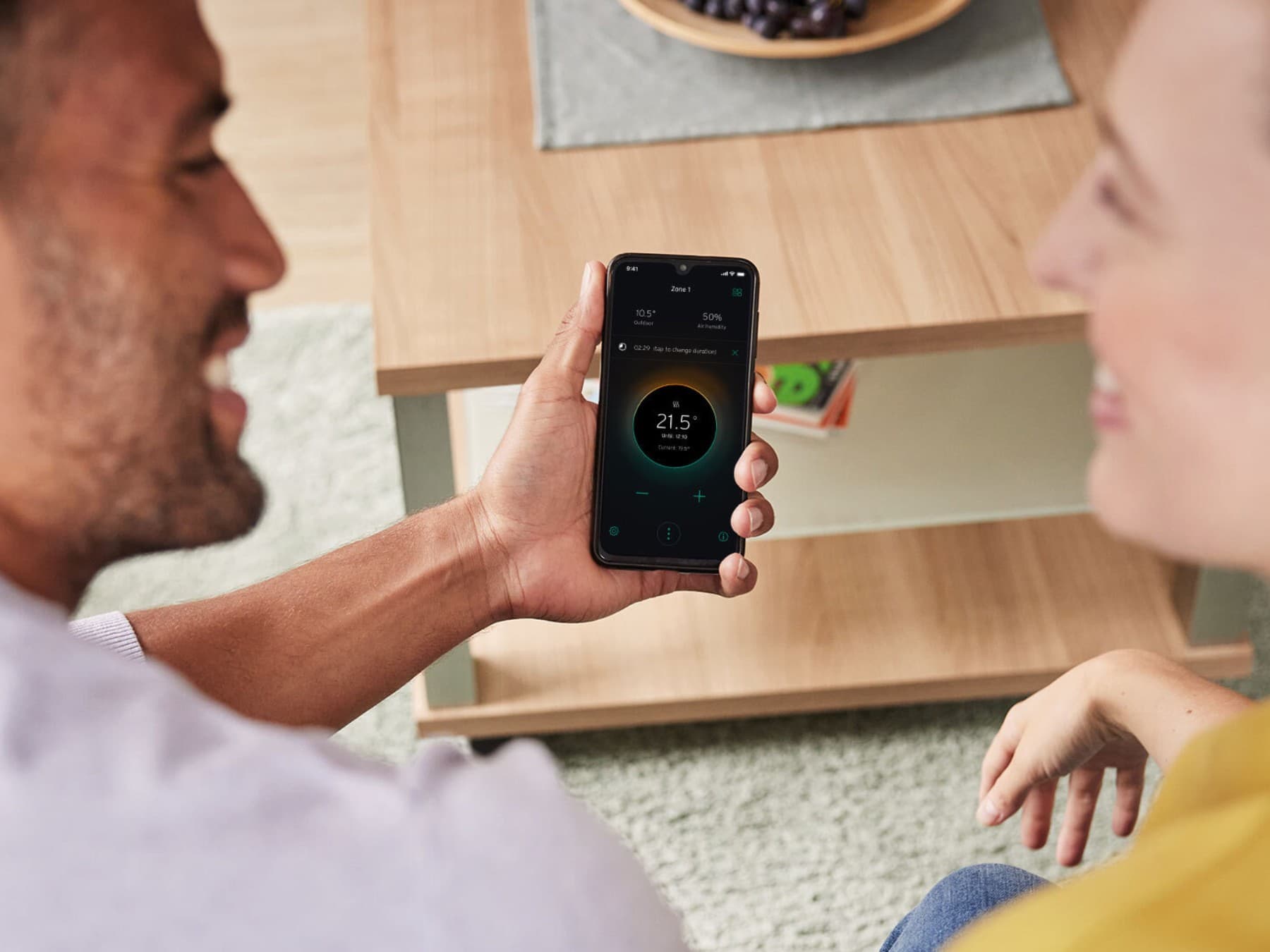 Ein Mann sitzt neben einer Frau, der die myVaillant App auf seinem Smartphone bedient.