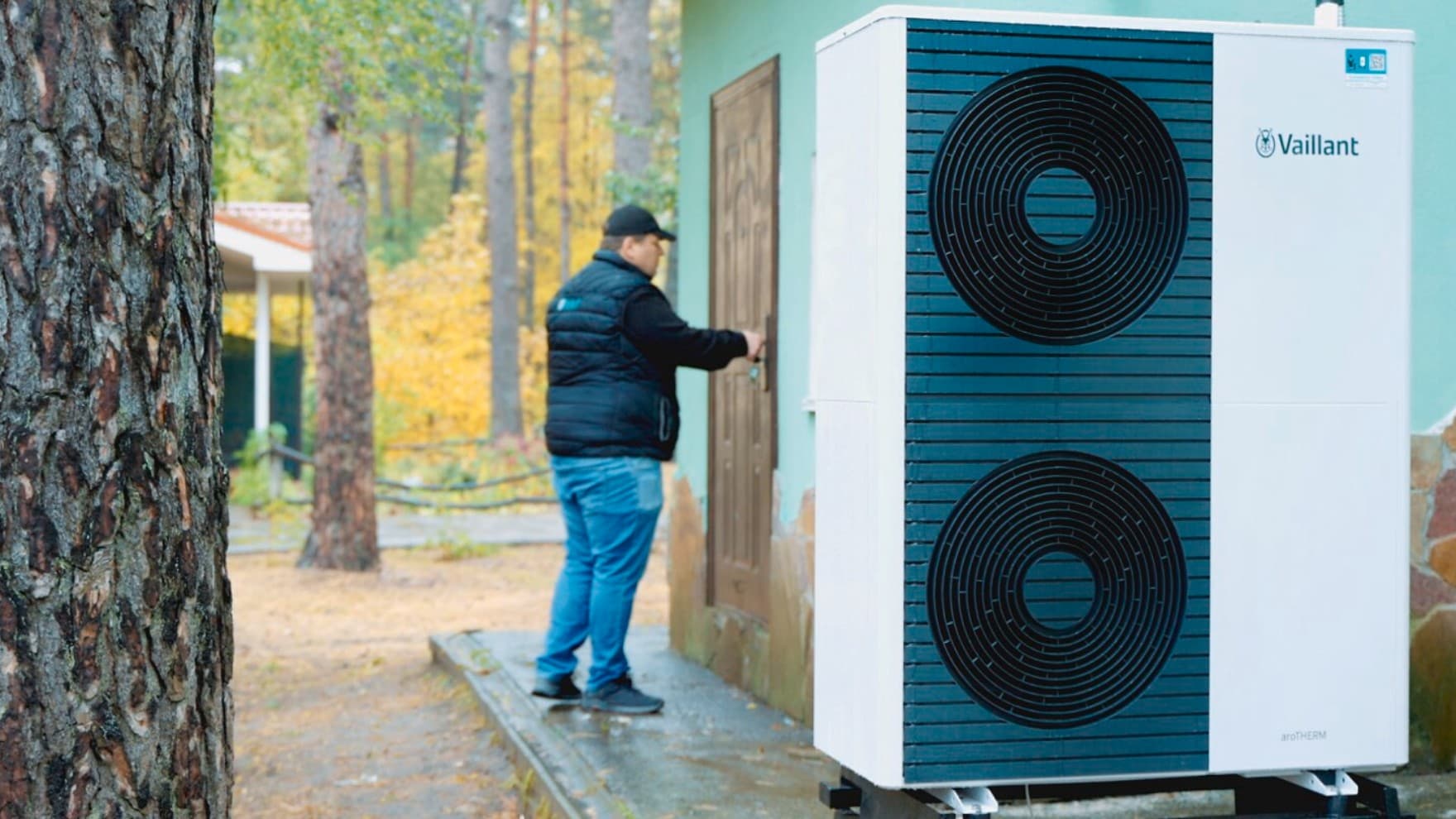 Ein Mann öffnet eine Holztür, im Vordergrund steht eine Vaillant Wärmpeumpe