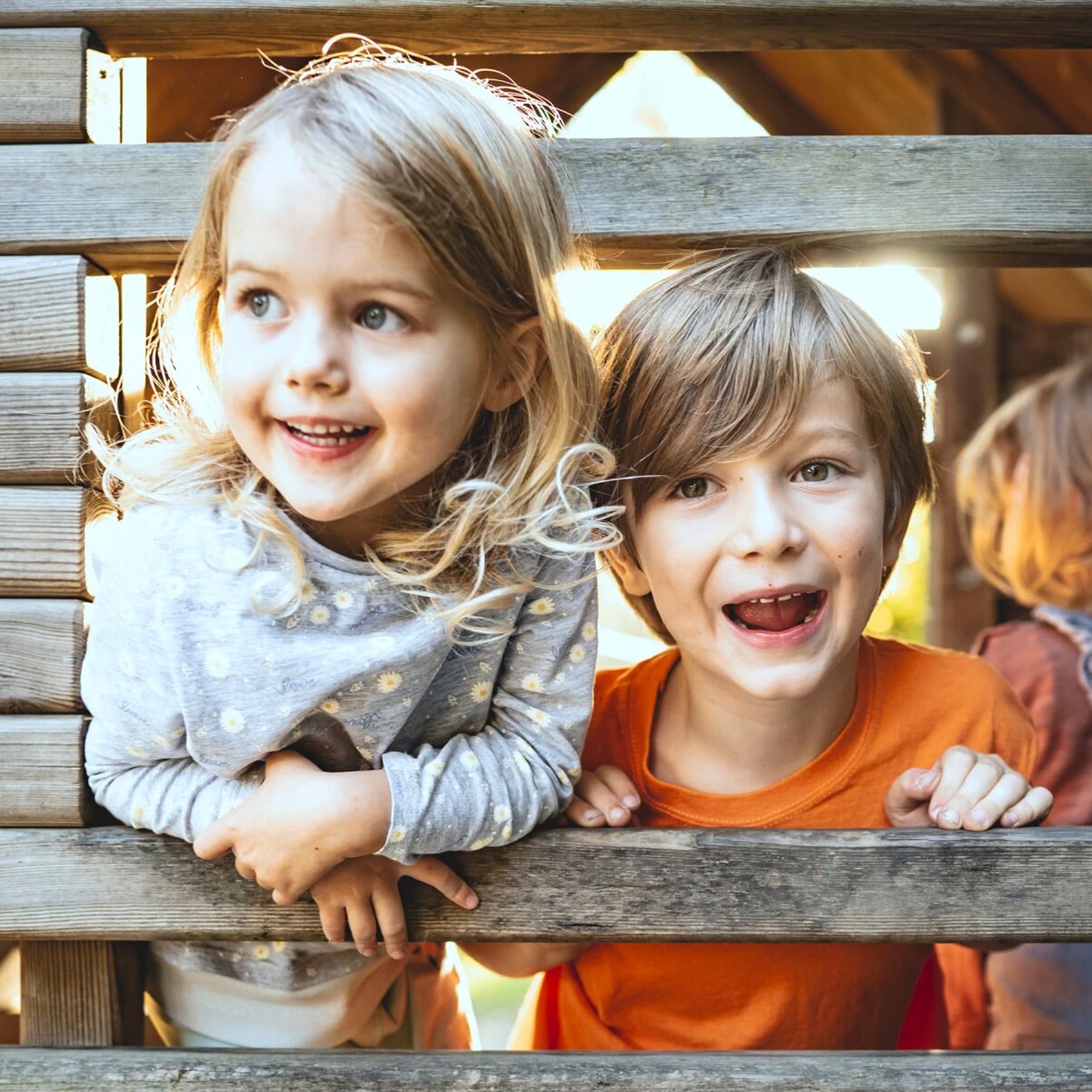 Zwei Kinder spielen in einer Holzhütte auf einem Spielplatz.
