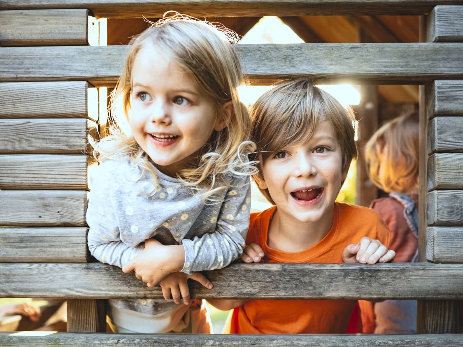 Zwei Kinder spielen in einer Holzhütte auf einem Spielplatz.